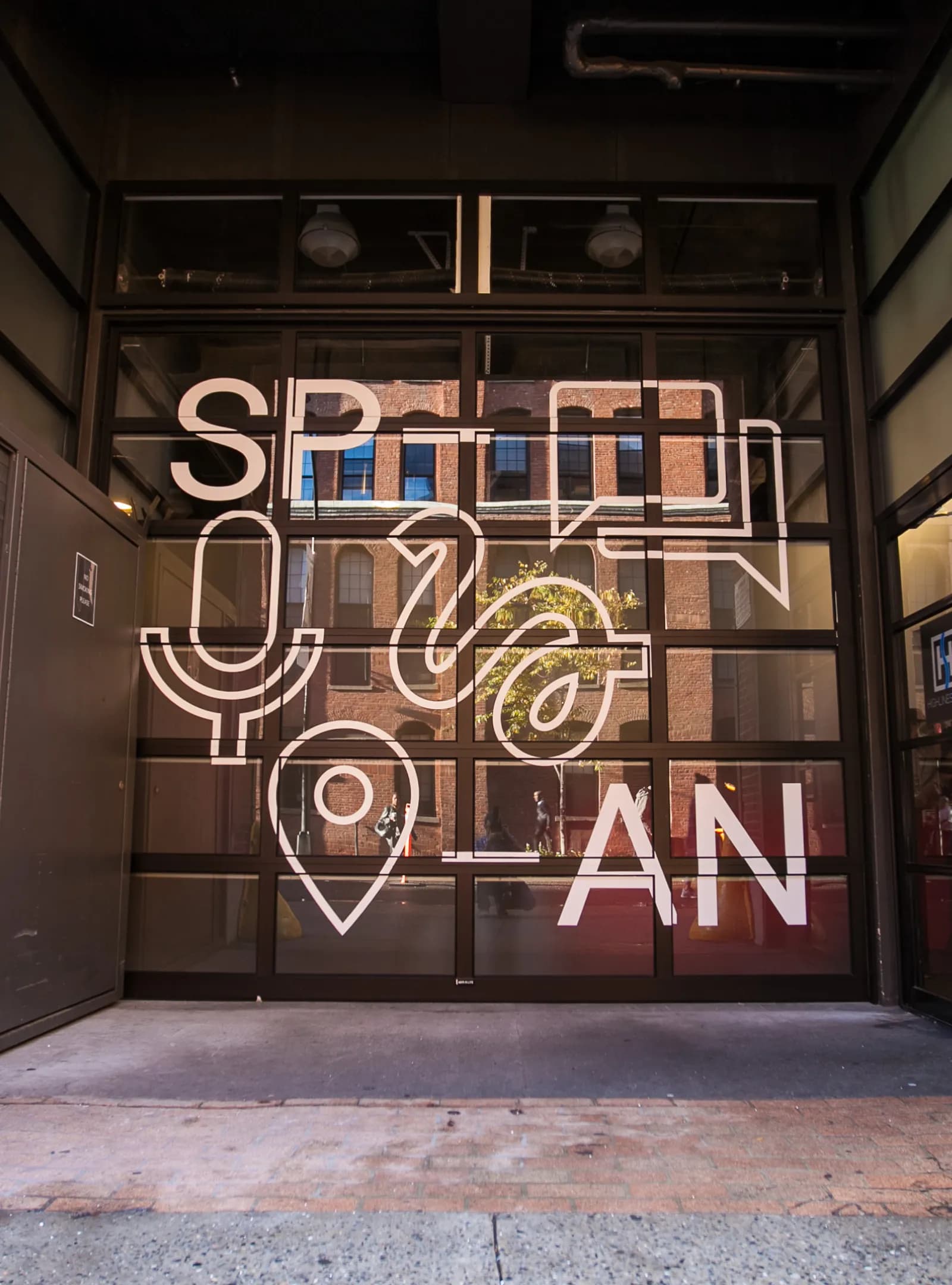 "Glass doors of a building reflect a brick edifice across the street. Large letters spell ""SPAN."" "