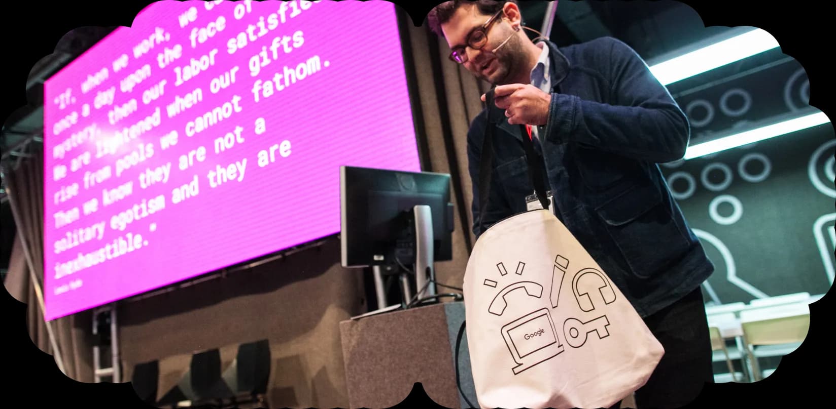 Rob adjusts a Google tote bag while standing near a large pink screen displaying an inspirational quote.