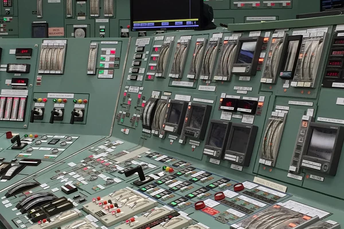 Complex control panel inside a nuclear power plant, featuring various switches, dials, and digital displays.