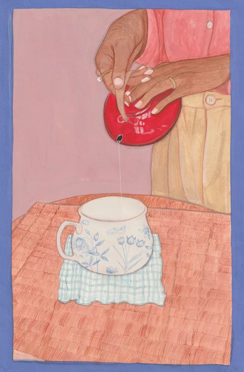 Brown hands pour milk from a red pot into a floral mug sitting on a checkered cloth upon an orange woven surface.