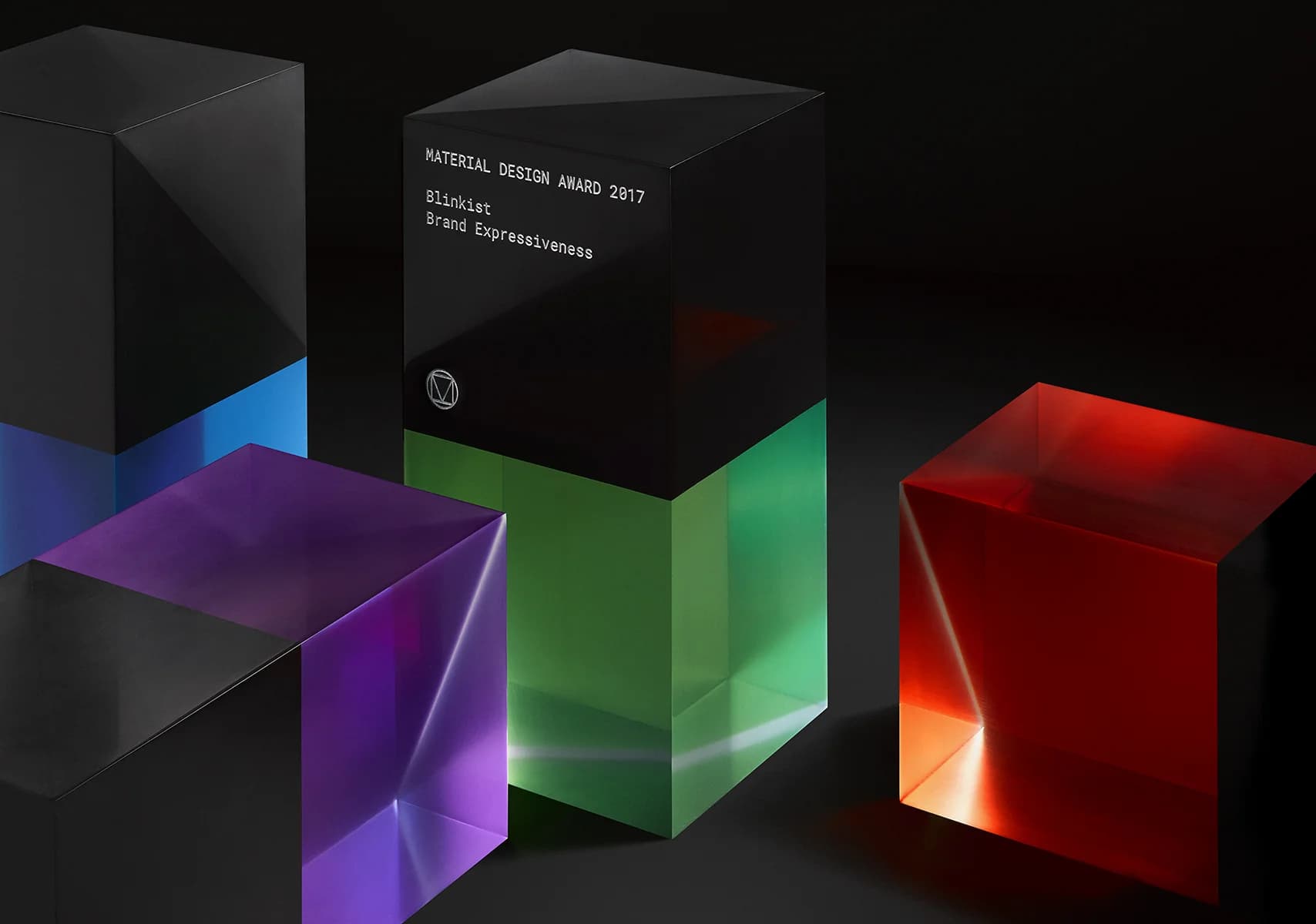Four Material Design Awards, black cubes with colorful translucent bases, sit on a dark surface. One green award reads, "Blinkist, Brand Expressiveness, 2017."
