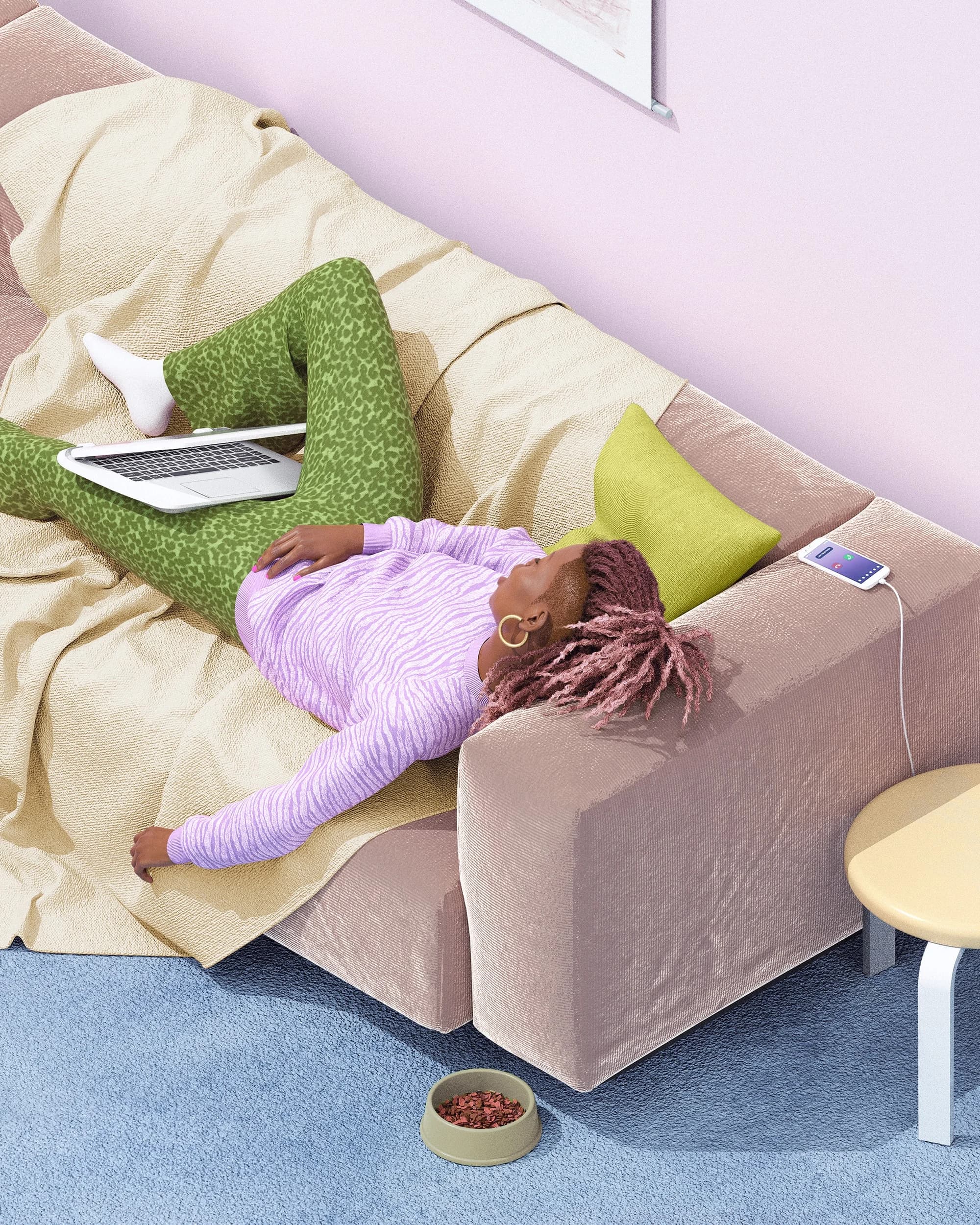 A person relaxes on a comfy couch, laptop resting on their lap. Their phone charges nearby, and a pet's food bowl sits on the rug below.
