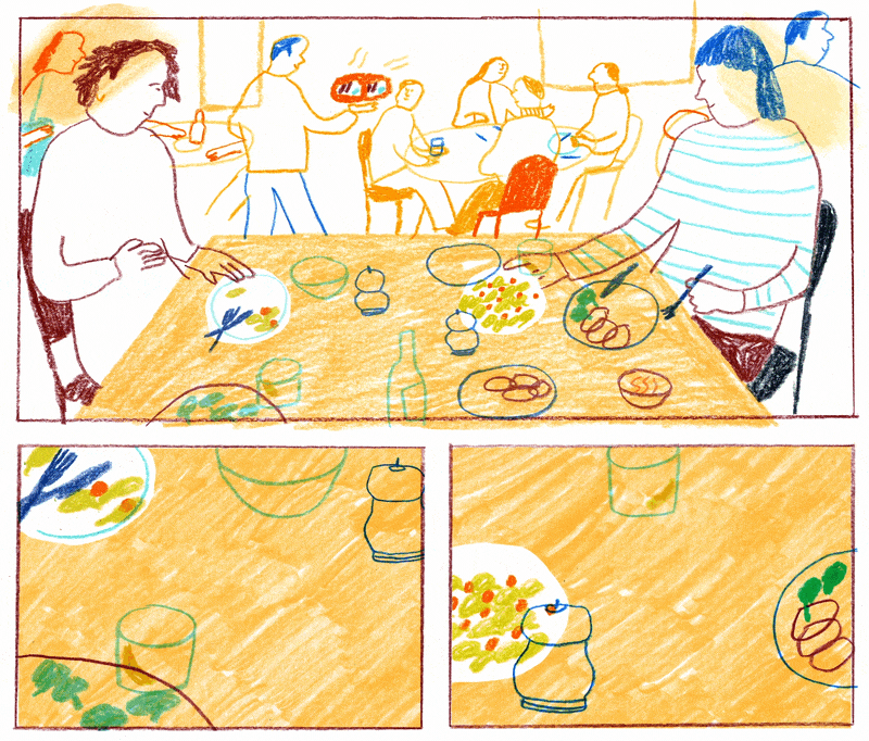 Two people sit at a table laden with food, facing a background of other diners.