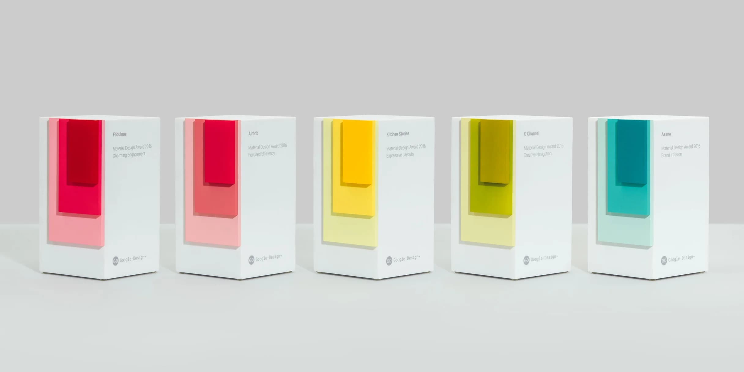 Five Material Design Awards from 2016, each a white rectangular prism with colorful layered accents.