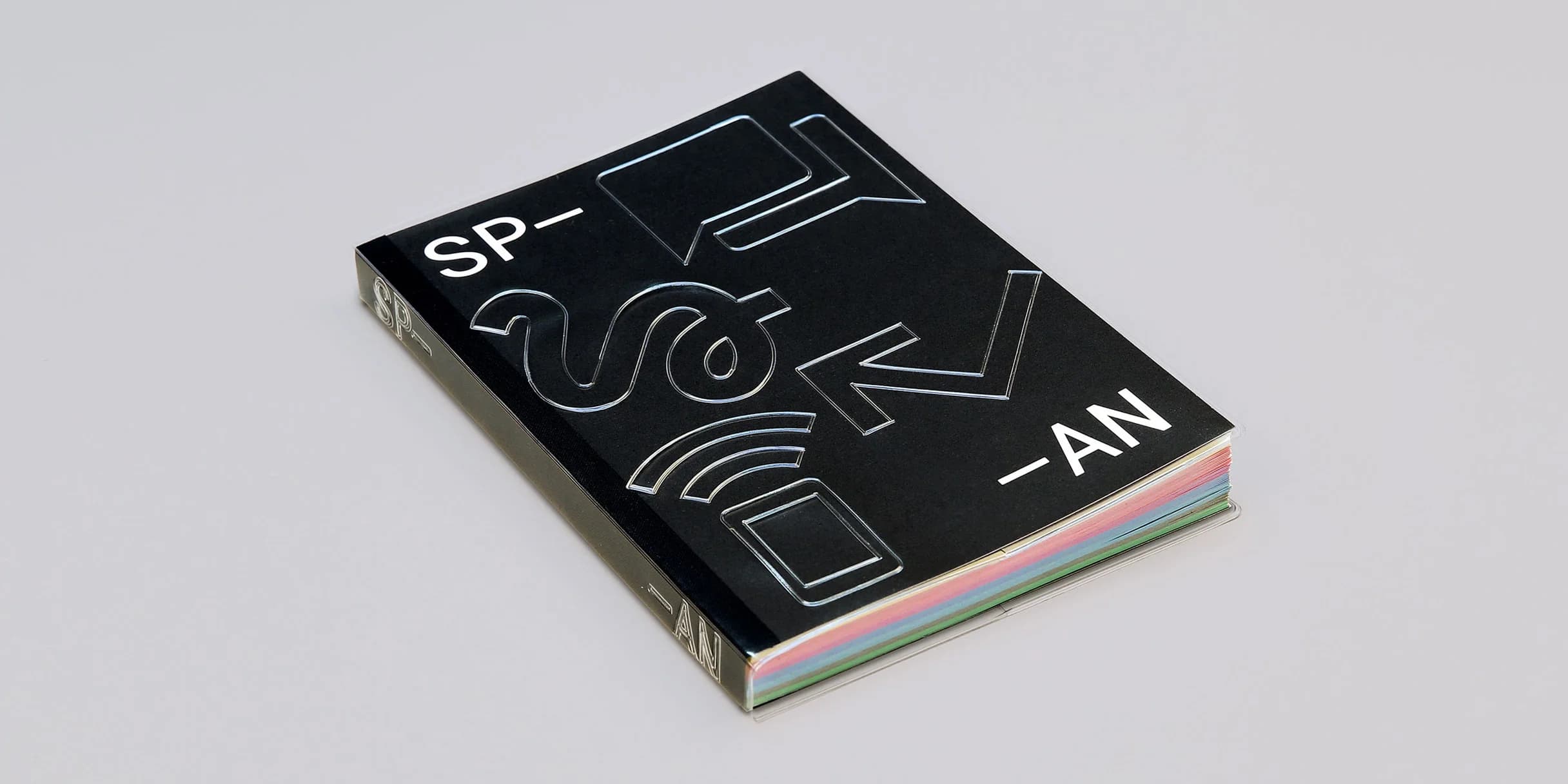 Black book cover with embossed, silver graphic elements. Title: SPAN. Colorful page edges peek through. Book rests on a light gray surface.