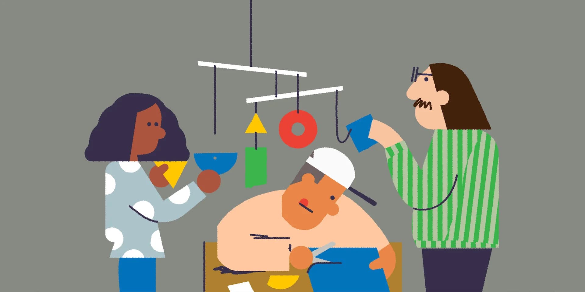 Three people assemble a colorful mobile with geometric shapes. One person cuts fabric, another holds a triangle, and the third hangs a blue shape.