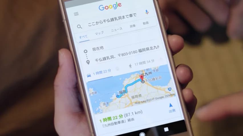 A hand holds a smartphone displaying Google Maps directions in Japanese.