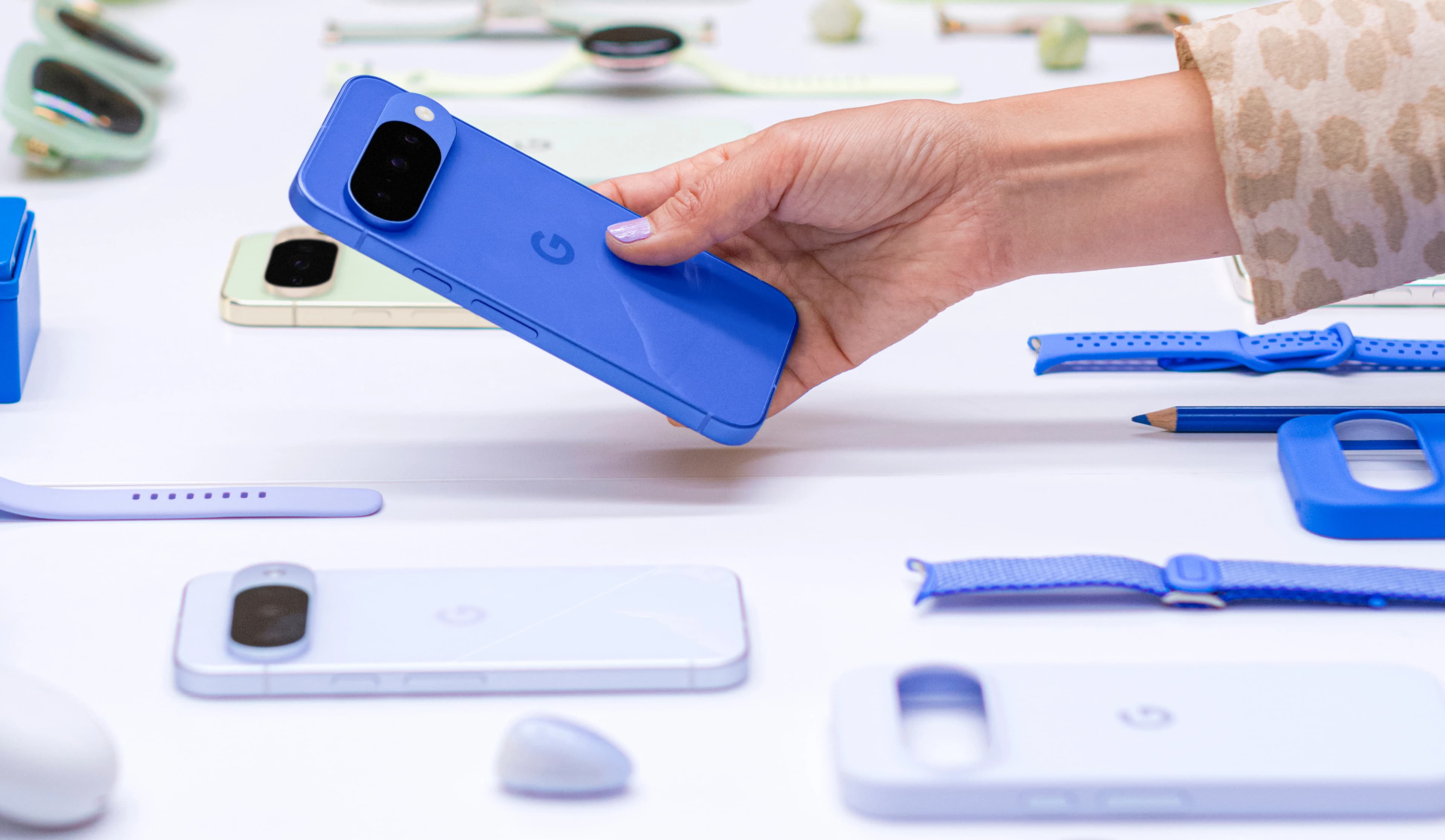 A hand holds a bright blue smartphone surrounded by other digital devices.