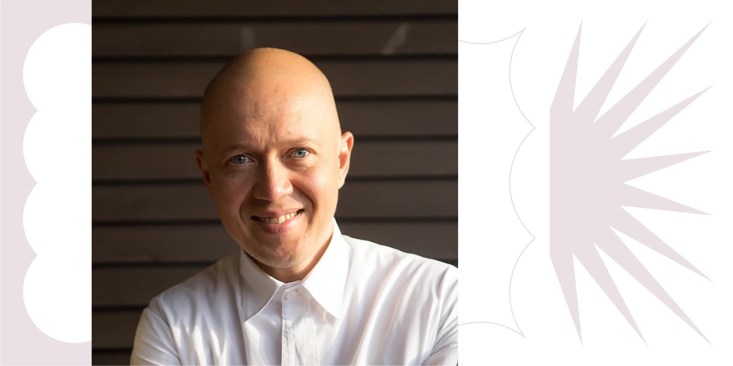 Smiling, bald man in a white, button-down shirt, stands against a brown, horizontal slat wall.