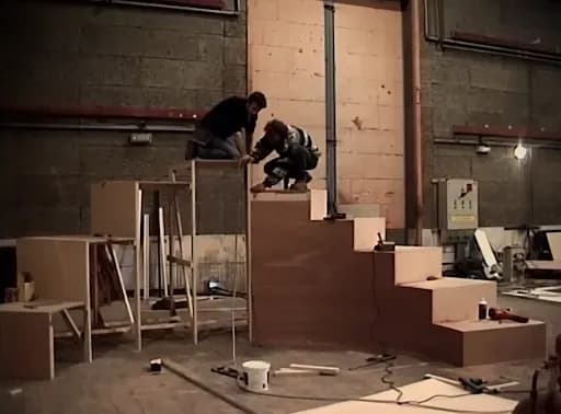 2 stagehands build the curved stairs used in the music video.