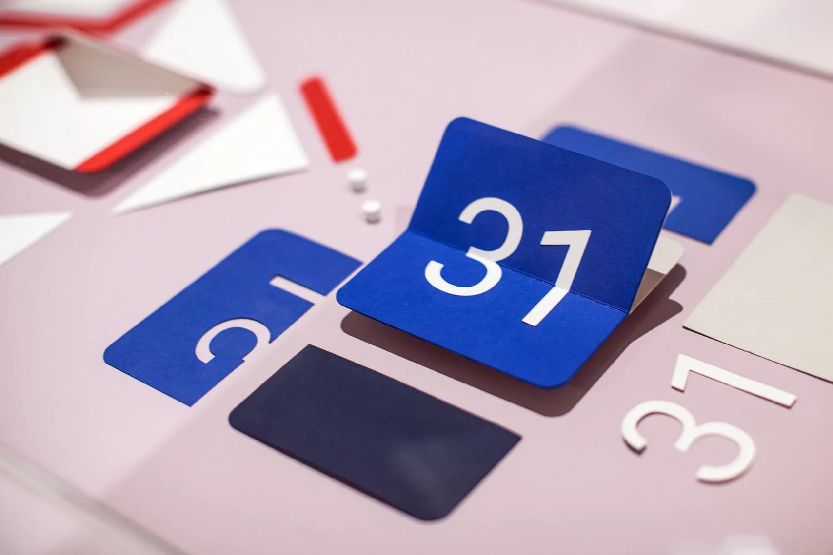 Blue and white paper number 31 on a pink surface with other paper shapes and numbers.